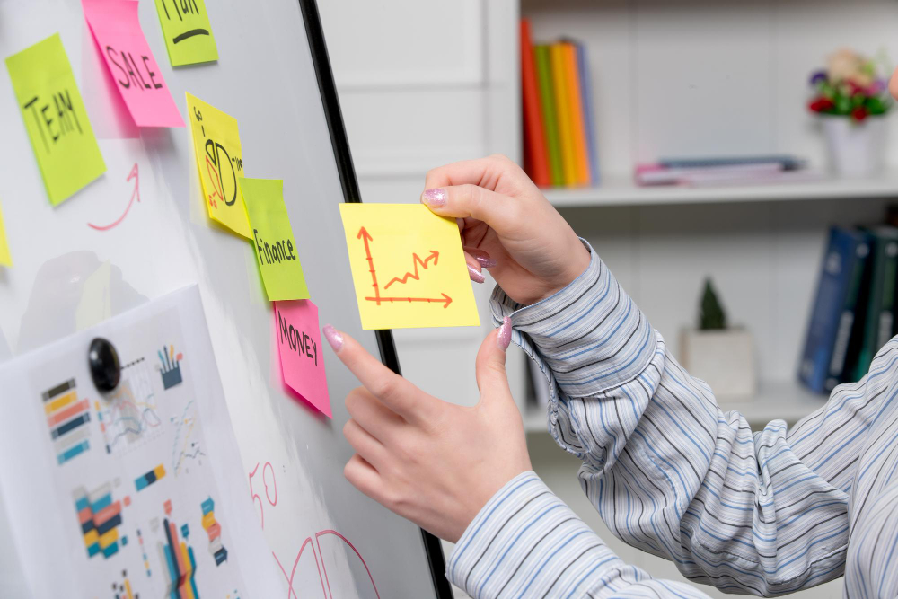 Person placing a sticky note with an upward graph on a whiteboard during a short OKR implementation planning session.